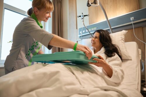 nurse giving patient food tray in hospital bed