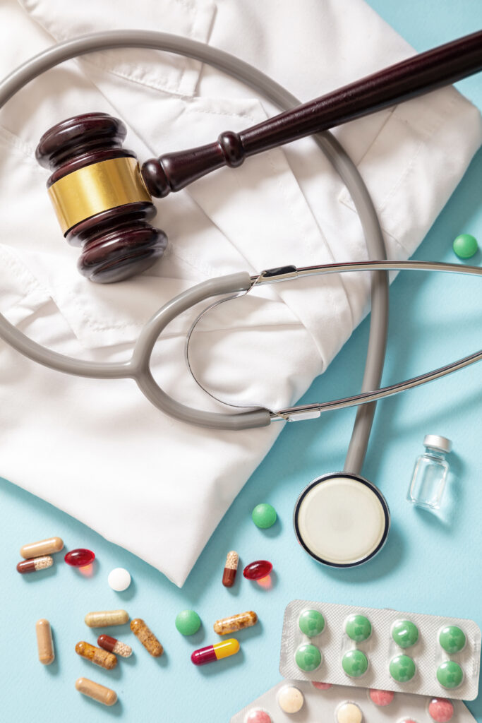 Judge gavel, stethoscope and medication on doctor coat, top view