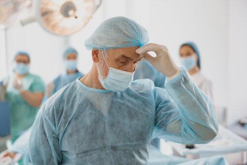 Close up of tired senior surgeon standing in operating room after hard unsuccessful operation
